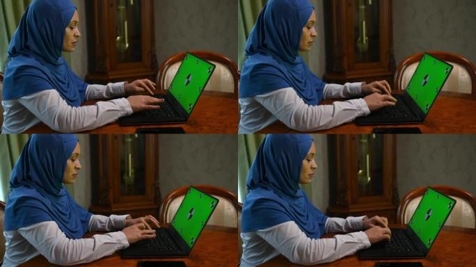 戴着头巾的勤奋的穆斯林妇女，在带有绿色色度键的笔记本电脑上远程工作。广告剪辑的模型屏幕