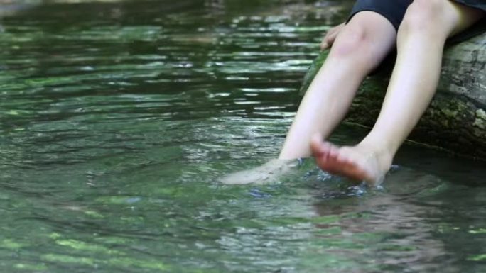 赤脚男孩用清澈的水和田园诗般的漂浮小溪在水中冷却他的脚在夏天展示了户外徒步旅行，在平静的小溪与家庭户