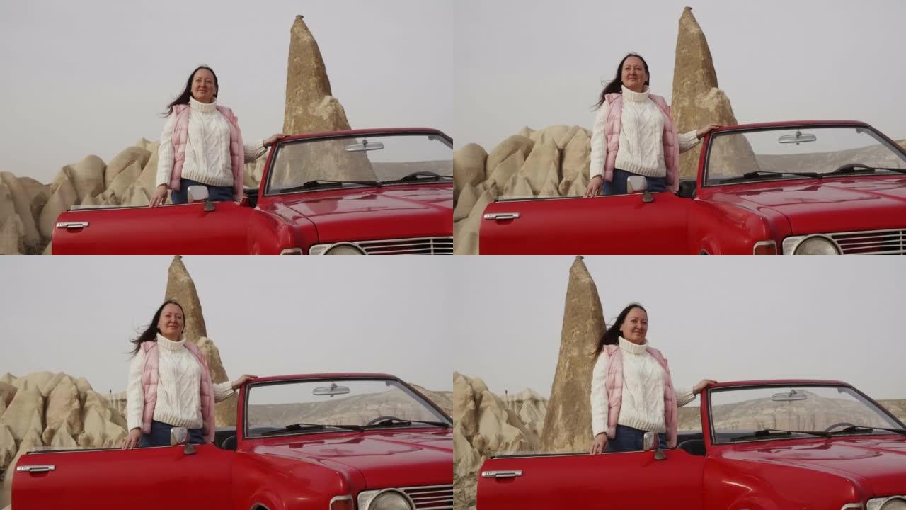 女人站在复古敞蓬车红色汽车旁，欣赏岩石。