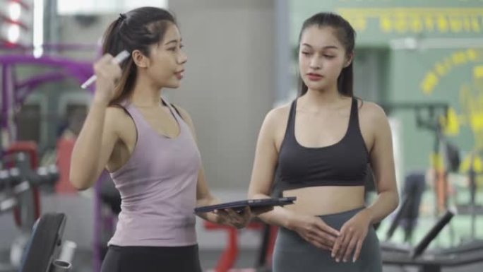 健身概念。亚洲女孩正在和一位推荐锻炼方法的女教练交谈。4k分辨率。