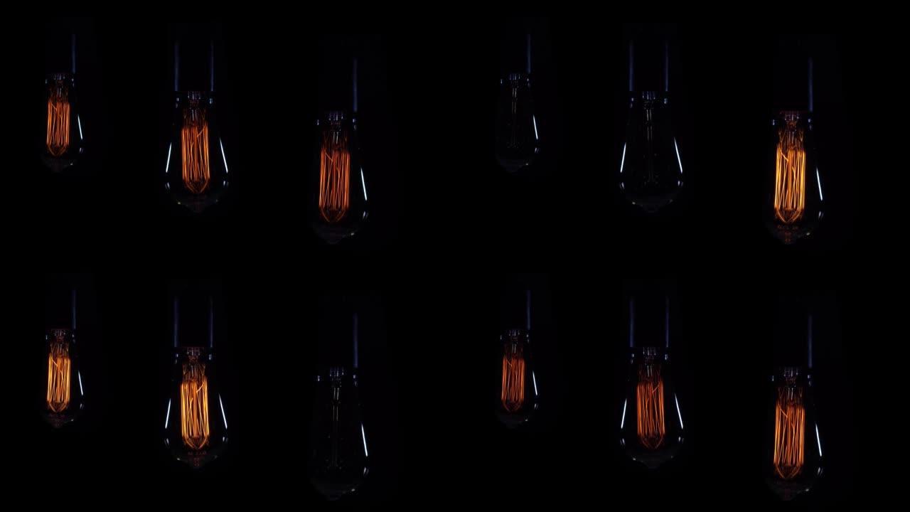 三个亮橙色螺旋复古风格白炽灯泡。黑色背景上的怀旧灯，可调光，打开和关闭电压。灯在摆动。