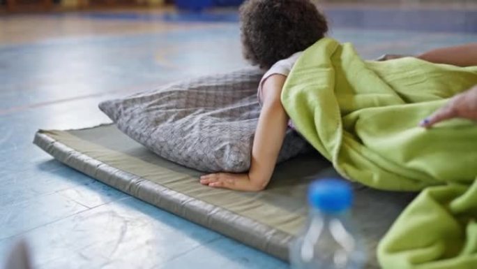 蹒跚学步的小女孩睡在紧急庇护所的床垫上