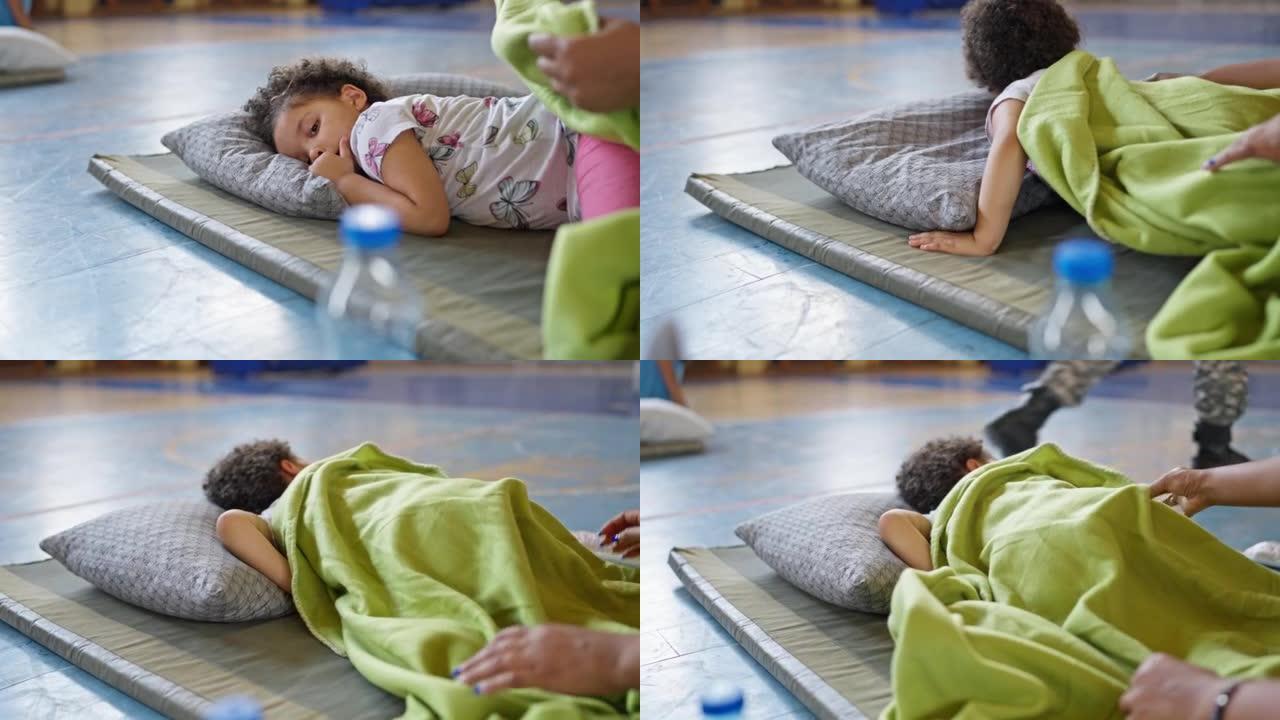 蹒跚学步的小女孩睡在紧急庇护所的床垫上