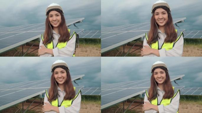 穿着制服的亚洲女工程师在太阳能电池板工厂工作，然后对着镜头微笑。