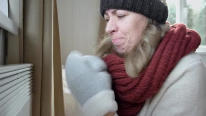 年轻的冷冻女人穿着一件毛衣在冬天的寒冷中颤抖着，脸上表情休克。女孩正在用电加热器呼吸。呆在家里不舒服