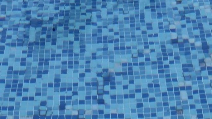 池底的苛性像灯笼波浪一样涟漪和流动。夏季背景。水面的质地。游泳池底部的瓷砖马赛克。