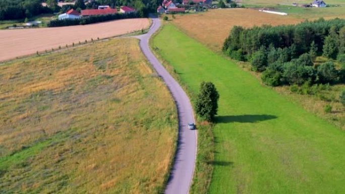 欧洲自然乡村乡村景观的公路旅行旅行度假。鸟瞰车在树木和农田之间的乡村道路上行驶。波兰乡村的房子村。