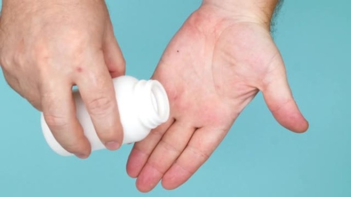 一只男人的手打开装有医用胶囊的瓶子，然后将药片倒入手掌。白色药物装在药瓶里和手里。医疗保健。药学和治