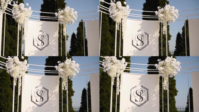 装饰婚礼拱门背景，新娘和新郎名字的首字母缩写。婚礼拱门装饰着白花，户外绿化。新婚夫妇的两个名字的首字