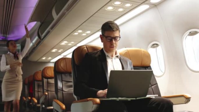 准备旅行时，使用笔记本电脑工作的商人坐在飞机上的4k视频片段。商务舱飞机的服务。出行安全。生活中的小