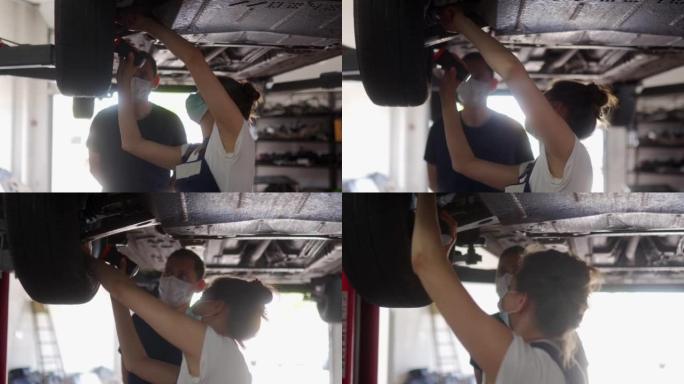 女机械师检查汽车悬架。强壮的女人执教一名男性实习生。工人在升降机上检查车辆的底部和行驶装置。因为检疫