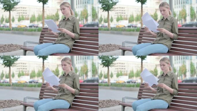 女人坐在户外长凳上阅读文件