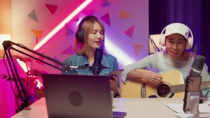快乐的亚洲女孩朋友影响者在笔记本电脑onair在线直播播放吉他一起为家庭工作室的追随者演唱歌曲。