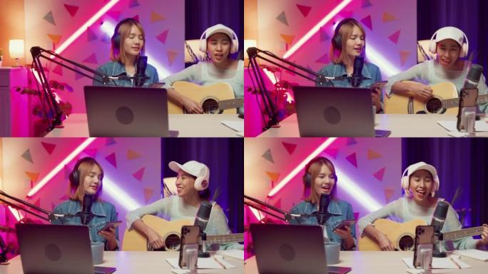 快乐的亚洲女孩朋友影响者在笔记本电脑onair在线直播播放吉他一起为家庭工作室的追随者演唱歌曲。