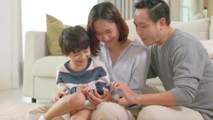 一个有学龄前儿童的幸福家庭正坐在现代托儿所的地板上玩智能手机，打视频电话，一起在家度过闲暇时光。播放