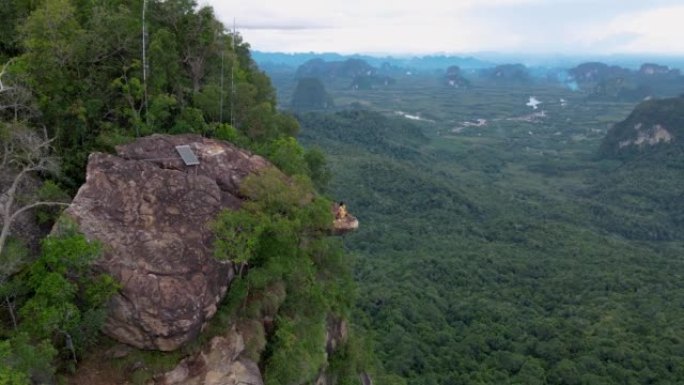 龙冠山泰国甲米，一个年轻的旅行者坐在悬在深渊的岩石上