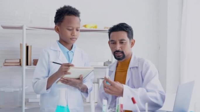 4K，大胡子的亚洲老师正在教混血男孩学生学习试管中的液体，并记下小学科学实验室里看到的东西。概念教育