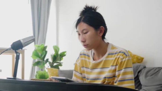 亚洲女孩通过移动应用程序学习弹奏键盘乐器，并在家里窗户附近的沙发上唱歌，生活方式概念。