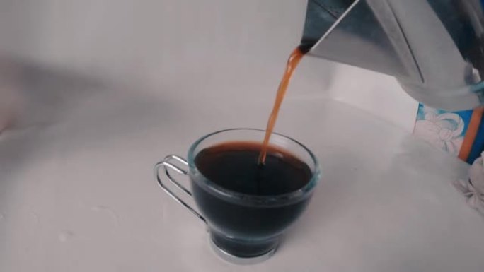 倒茶，在杯子里倒黑咖啡的超级慢动作镜头。从间歇泉咖啡机倒入杯中的咖啡的俯视图。