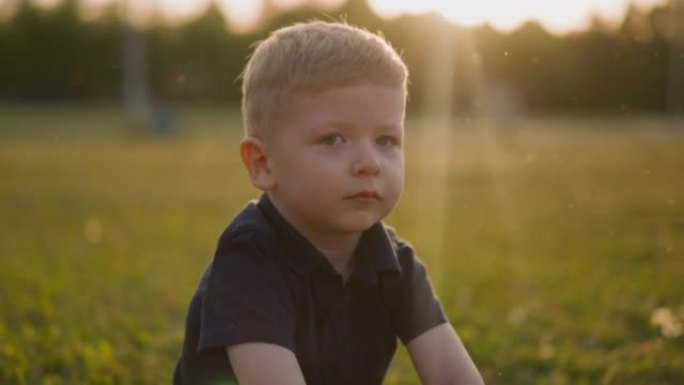 Upset little boy in black clothes sits on lawn at 