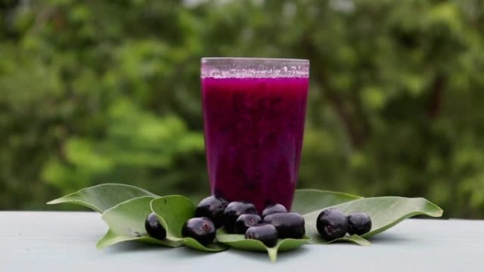 在带有复制空间的木制背景上隔离的水果和叶子的玻璃杯中的Jamun或黑梅汁，也称为Malabar Pl