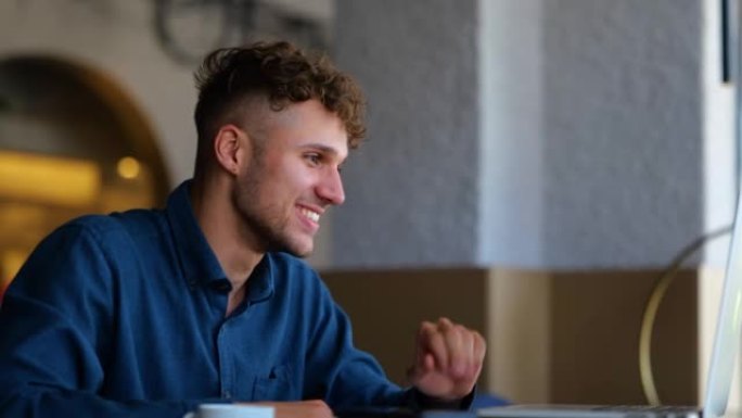 快乐的年轻白人男子微笑着挥手看着笔记本电脑屏幕，并在餐厅在线聊天。有视频会议的帅哥。休闲。慢动作