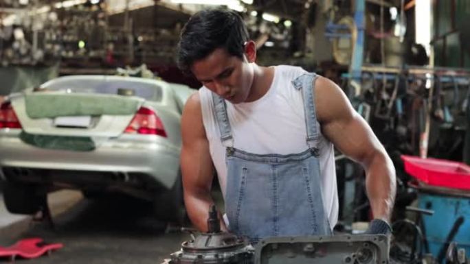 亚洲男性汽车工程师在旧工业汽车车库车间固定发动机动力传动齿轮箱