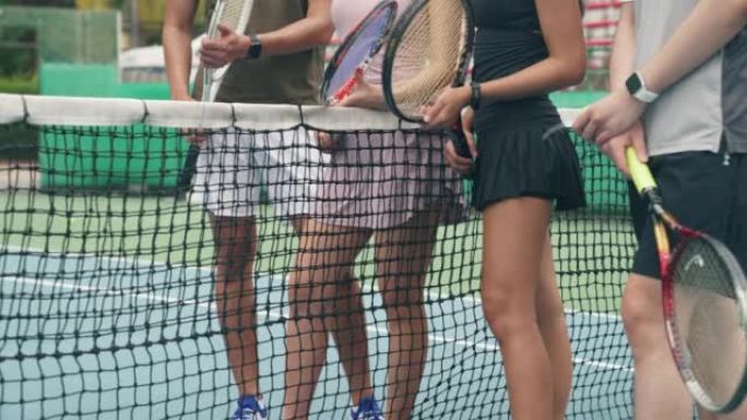 四个亚洲人聚集在网球场网上聊天。