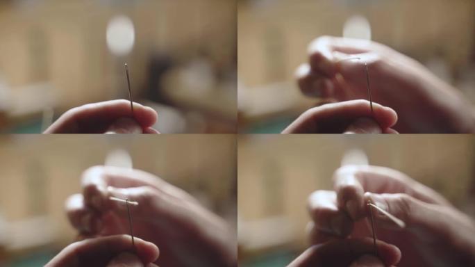 特写男性手穿针。缝纫和裁缝的操作细节。男人的手指使用背景模糊的针和线。