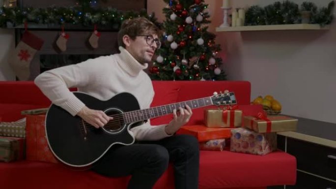 男人正在装饰圣诞树附近的吉他上弹奏快乐的歌曲。