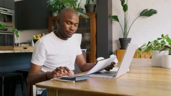 房屋贷款，账单或财务文件由一名非洲男子独自在家里的桌子旁用笔记本电脑分类。一个黑人在桌子上用纸计算，