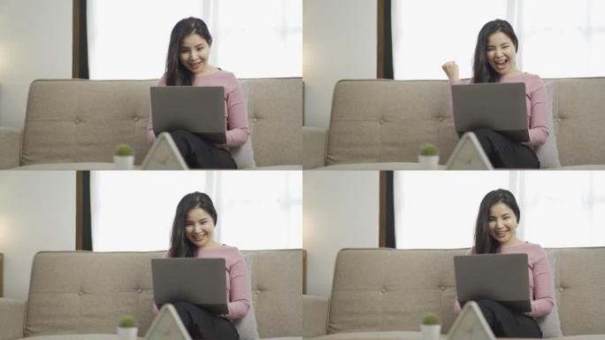 亚洲女人坐在沙发上，膝上放着笔记本电脑，打字而不是表现出快乐的表情，兴奋的女人看着笔记本电脑上的网上