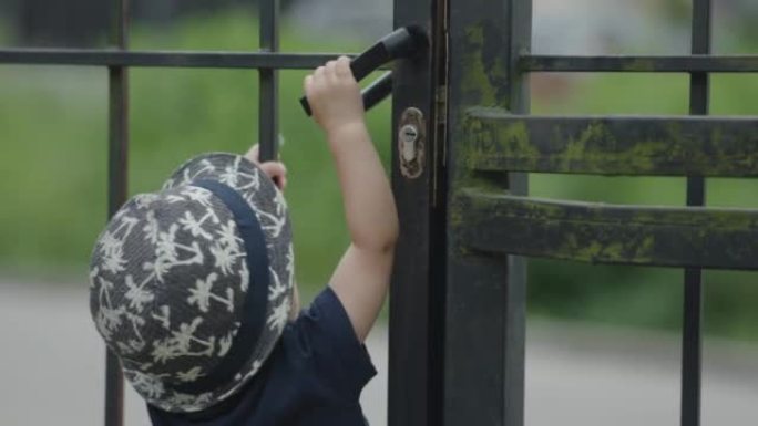 小婴儿蹒跚学步的孩子试图打开铁门门，门拿着黑色把手