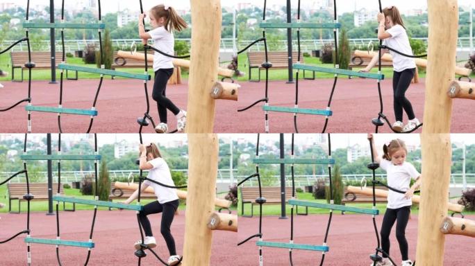 一个快乐的小女孩正在一个由木头制成的现代运动场上的绳索障碍赛道上攀爬。灵巧的发展