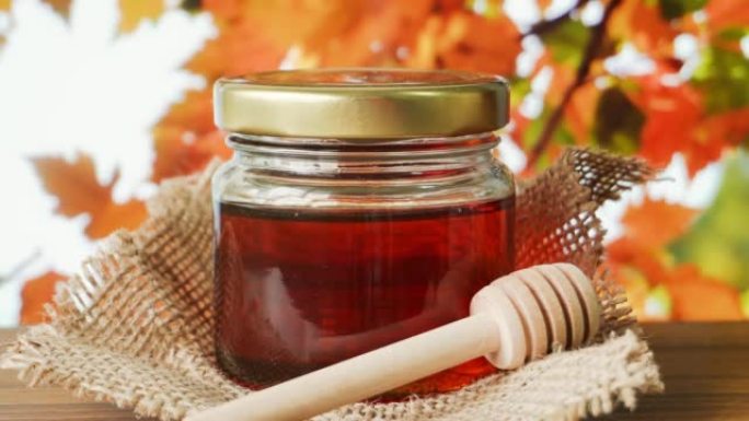 在木桌上放有蜂蜜北斗七星的玻璃罐中的蜂蜜，背景是秋天的叶子。