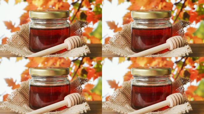 在木桌上放有蜂蜜北斗七星的玻璃罐中的蜂蜜，背景是秋天的叶子。