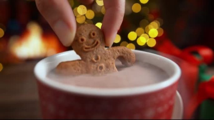 慢动作将姜饼人饼干浸入一杯热巧克力中，在壁炉旁休息圣诞节