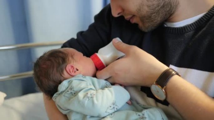 年轻的父亲第一次享受用奶瓶喂他刚出生的女婴，在她出生几天后去妇产医院看望她