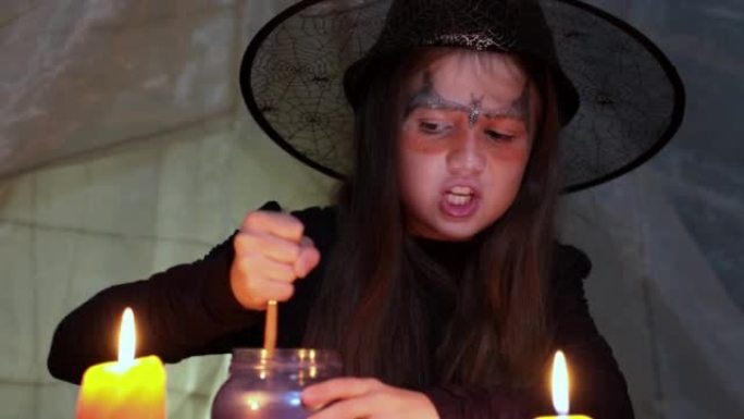 戴巫婆帽子的小女孩正在用蜡烛制作魔法药水和阅读咒语
