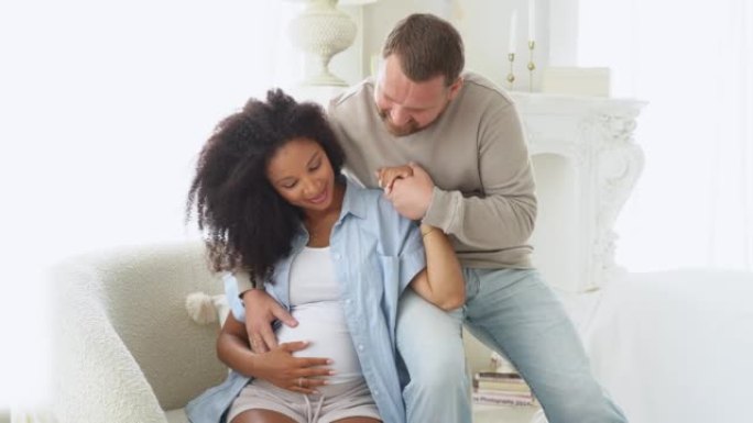 快乐怀孕的多民族夫妇在卧室拥抱。黑人孕妇和白人丈夫在家里的沙发上放松时摸着肚子。