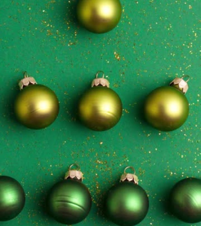 另类的绿色和黄色圣诞球在翡翠绿色的背景上制成带有金色闪光的树。停止运动垂直动画圣诞假期和呈现概念平铺