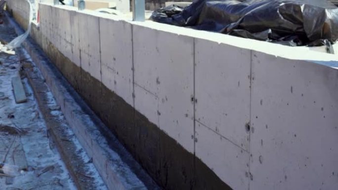 一名工人在混凝土挡土墙上浇筑混凝土搅拌模板。用胶合梁建造现代木屋。混凝土基础用沥青膜防水。