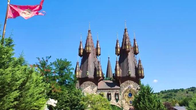 幻想宫殿，黑色和金色的尖塔，在森林林间空地的树木后面，挥舞着史诗般的旗帜-童话中拉瓦迪诺沃中世纪城堡