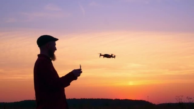 一个控制无人机飞行进行侦察的人的剪影。无人机在明亮的日落天空中左右移动。使用新技术的概念。