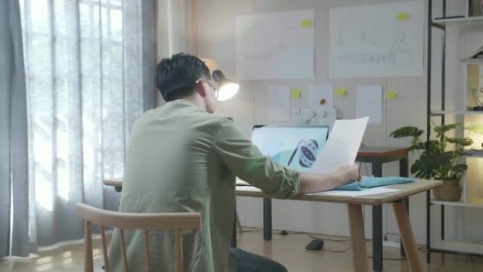 在办公室使用笔记本电脑设计袋子时，用织物看着布局结合的男包设计师的后视图