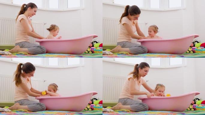 妈妈洗澡小女儿洗她的背宝宝玩水把她的杯子变成面对妈妈。