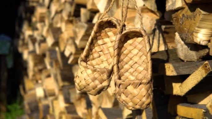乡村乡村概念。柳条桦木树皮韧皮鞋挂在木柴的背景上。