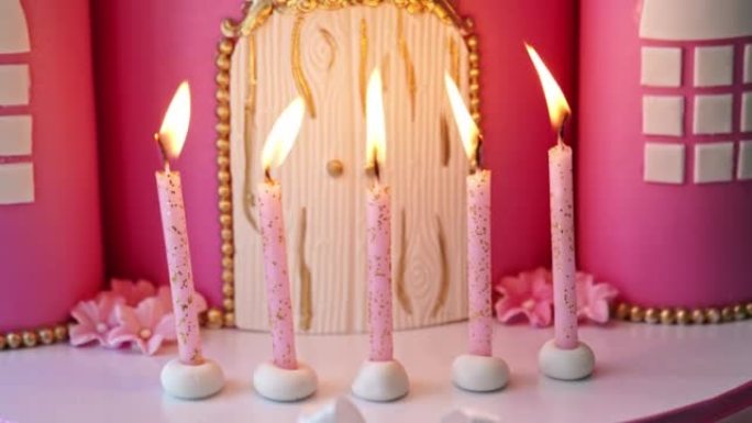 蛋糕上有五支燃烧的粉红色蜡烛，呈童话般的城堡。