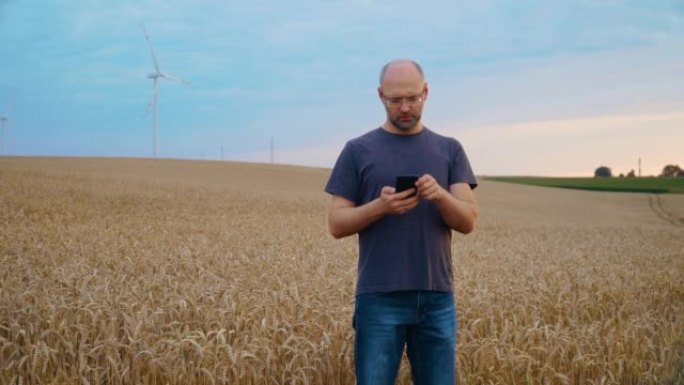 农民用智能手机在农业成熟麦田进行在线农业采购，背景是风车涡轮机