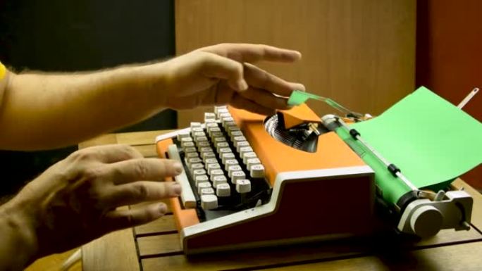 男性手在打字机上打字。橙色复古机械旧。绿皮书。